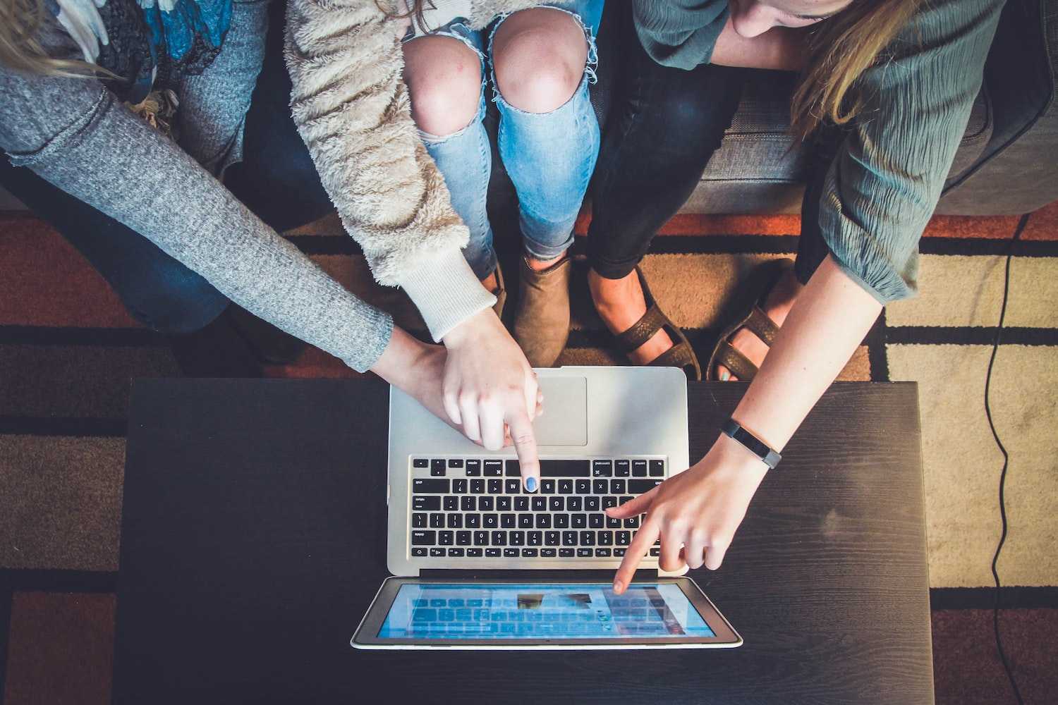 Two people pointing at a macbook